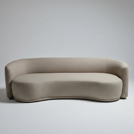 A curved, low-profile upholstered sofa in a textured taupe-beige fabric, photographed in a large furniture showroom or warehouse with other sofas and people visible in the background.