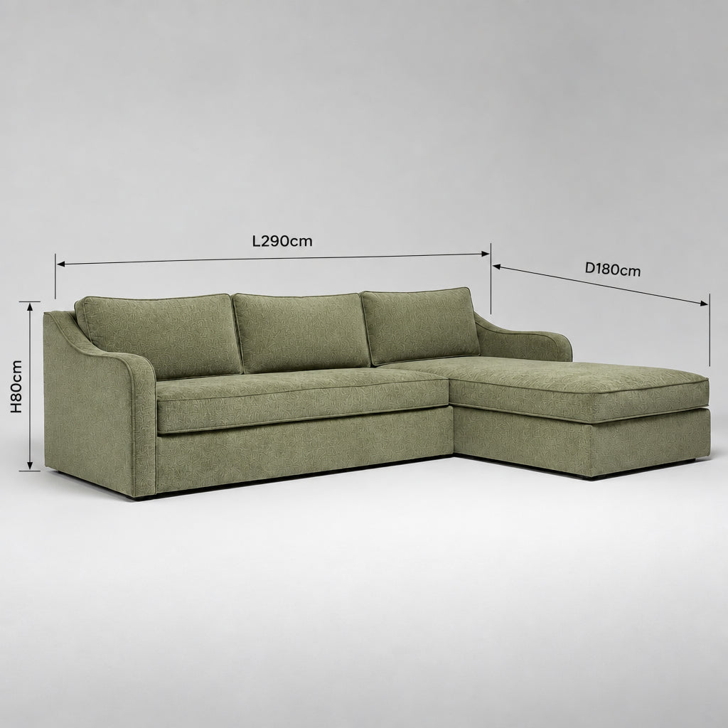 An L-shaped sectional sofa with a chaise lounge, upholstered in a textured sage green fabric, photographed in a warehouse or furniture showroom setting.