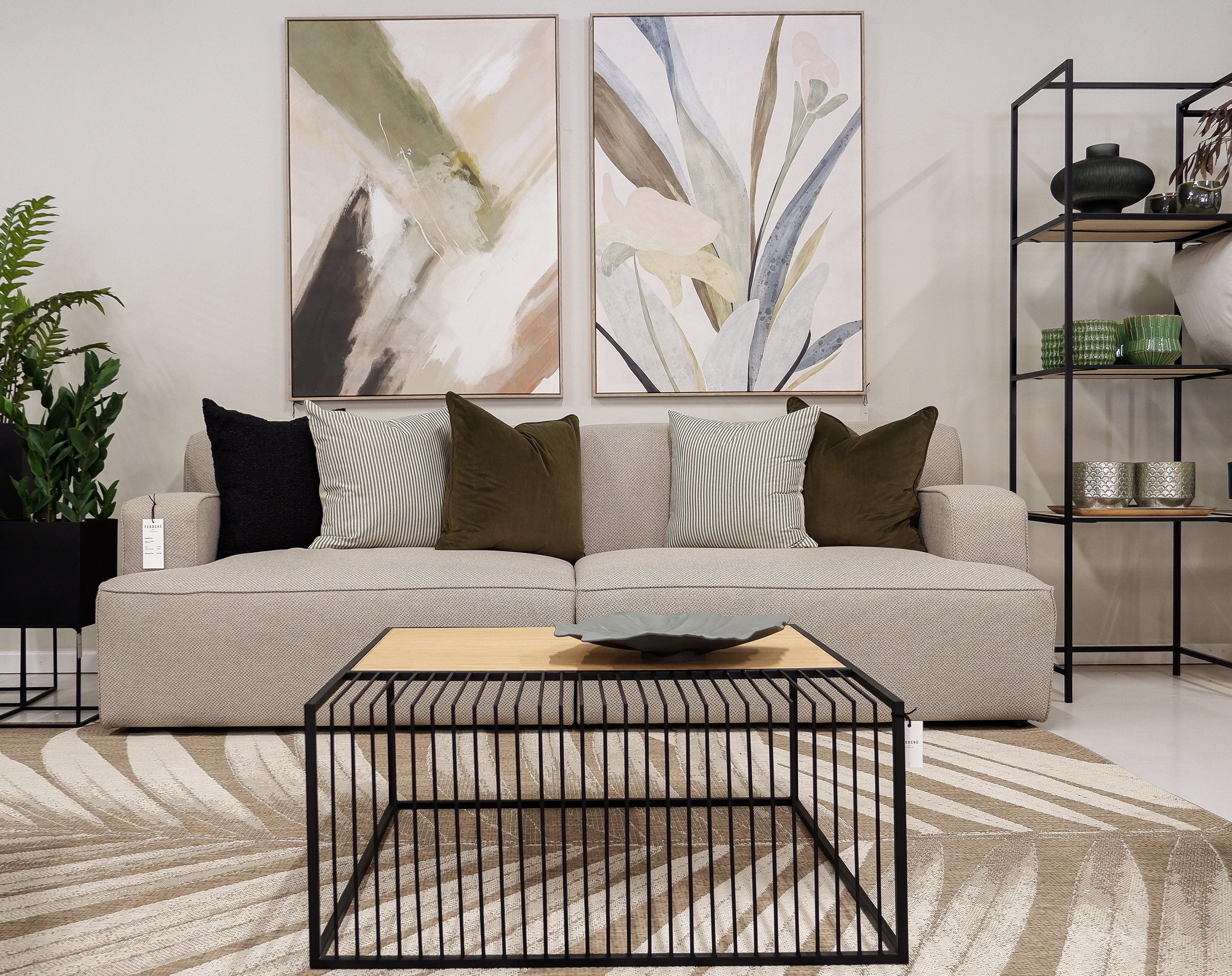 A beige three-seater sofa with decorative cushions, placed in a well-decorated living room setting with a modern coffee table, shelves, and wall art.