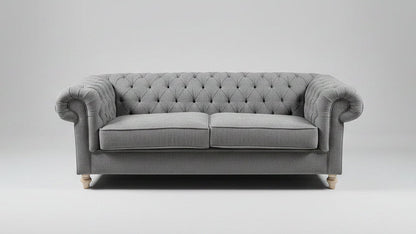 A gray tufted loveseat sofa with patterned throw pillows, styled in a showroom with a distressed blue-gray area rug, a small round coffee table, and a mustard yellow armchair.