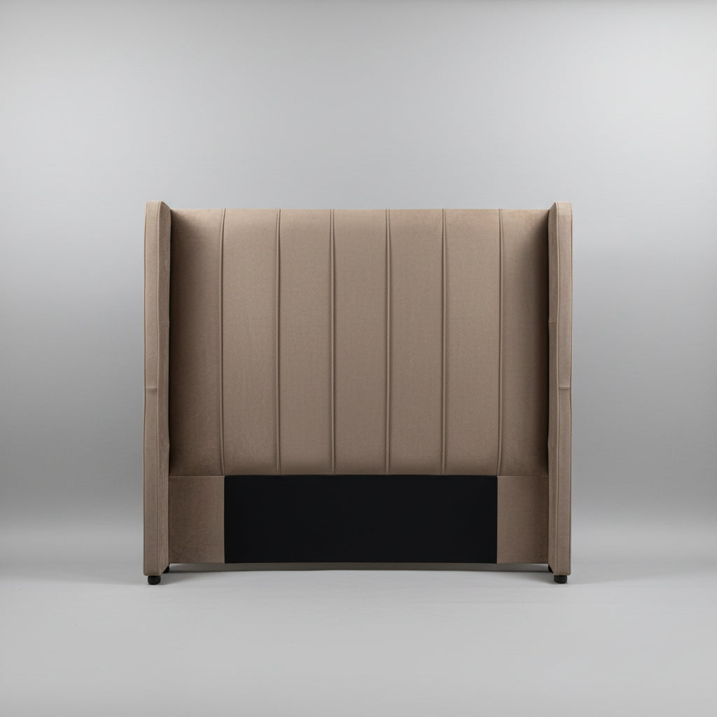A tall upholstered headboard with vertical channel tufting and wingback sides, shown standing against a light gray wall on a tiled floor.