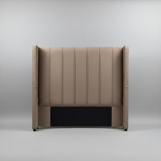 A tall upholstered headboard with vertical channel tufting and wingback sides, shown standing against a light gray wall on a tiled floor.