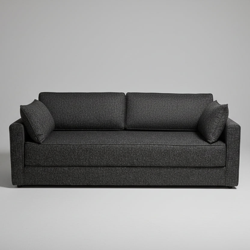 A dark gray textured fabric loveseat sofa with two matching back cushions, positioned in a retail showroom with baby furniture and bedding visible in the background.