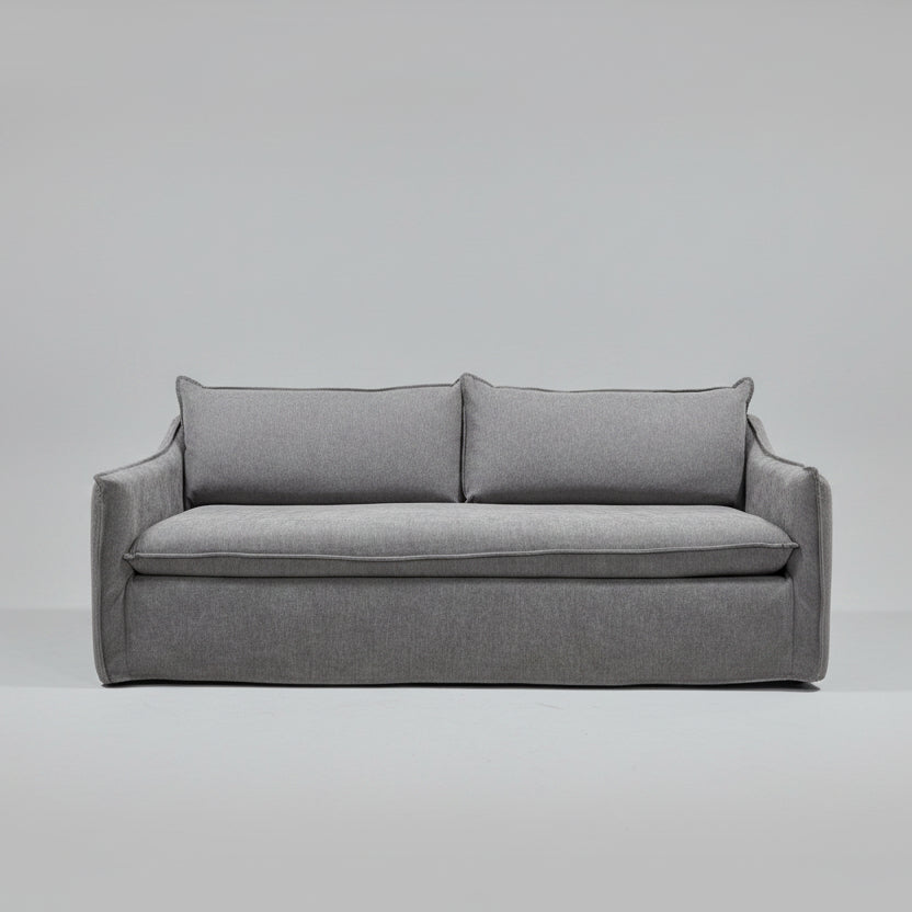 A gray upholstered loveseat or sofa with two back cushions and a thick seat cushion, photographed in a furniture store showroom with shelving and other furniture visible in the background.