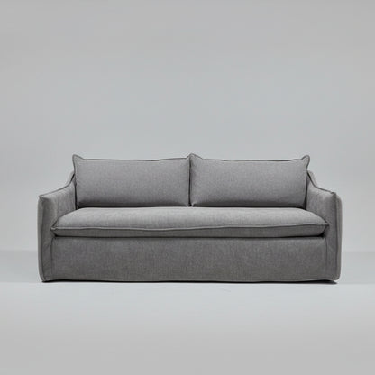 A gray upholstered loveseat or sofa with two back cushions and a thick seat cushion, photographed in a furniture store showroom with shelving and other furniture visible in the background.