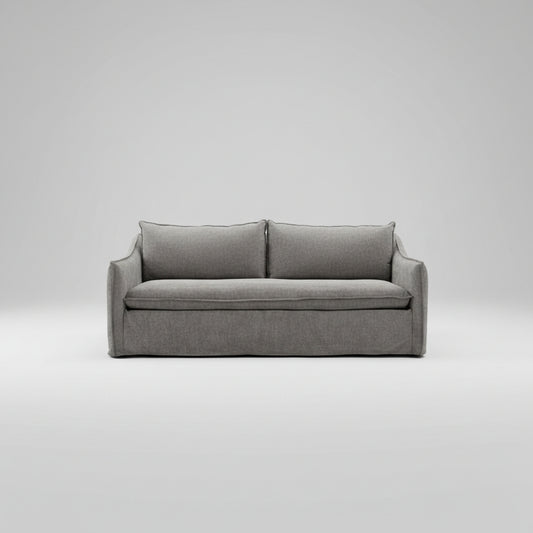 A gray upholstered slipcovered loveseat sofa in a warehouse showroom setting.