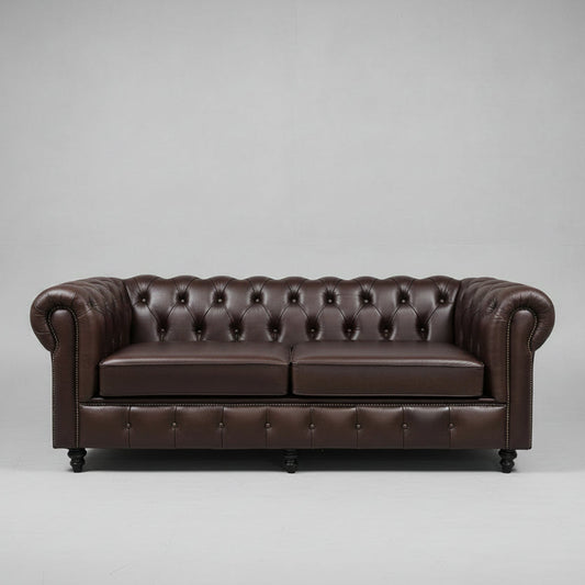 A dark brown leather Chesterfield sofa with button tufting, styled with two decorative throw pillows, set in a modern living room with a large organic-shaped wall mirror behind it.