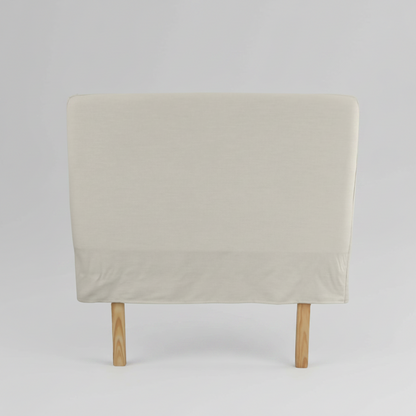 Beige slipcover headboard with wooden legs on a light grey background