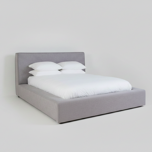 Gray upholstered bed with white bedding on a plain background