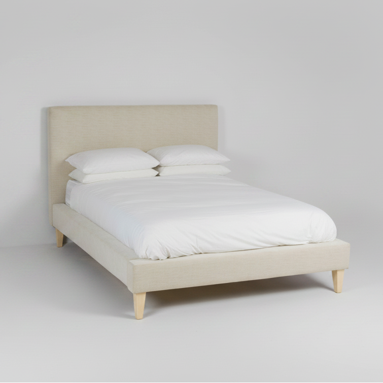 Beige upholstered bed with white bedding on a plain background