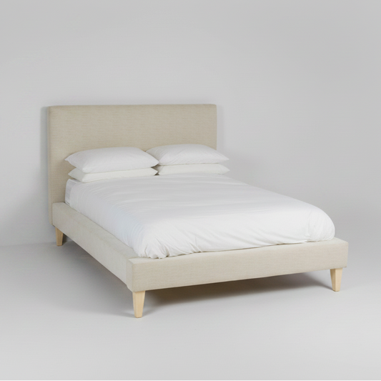 Beige upholstered bed with white bedding on a plain background