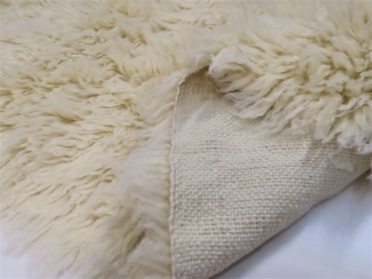 Close-up of a fluffy white rug and a textured beige pillow on a white surface.