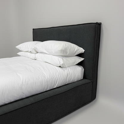 Black upholstered bed frame with white bedding and pillows against a gray background
