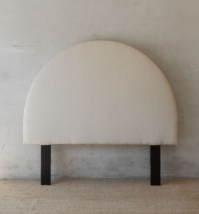 Round, beige headboard with black legs against a plain wall.