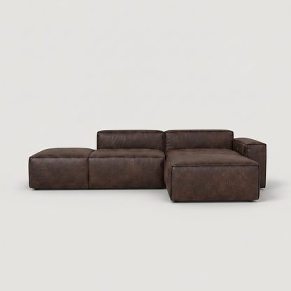 A dark brown modular sectional sofa with a chaise lounge on the left, shown against a plain light gray studio background.